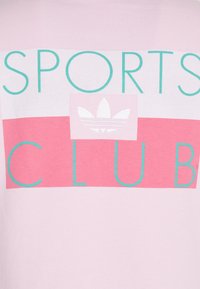 Světle růžové bavlněné tričko s výrazným nápisem "SPORTS CLUB" v tyrkysové barvě a malým bílým logem Adidas uvnitř růžového obdélníkového designu.