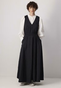 Pikk must kleit, millel on V-kaelus, elastne vöökoht ja küljetaskud. Seljas valge puff-sleeve särk ja kombineeritud valgete tennisetossudega.