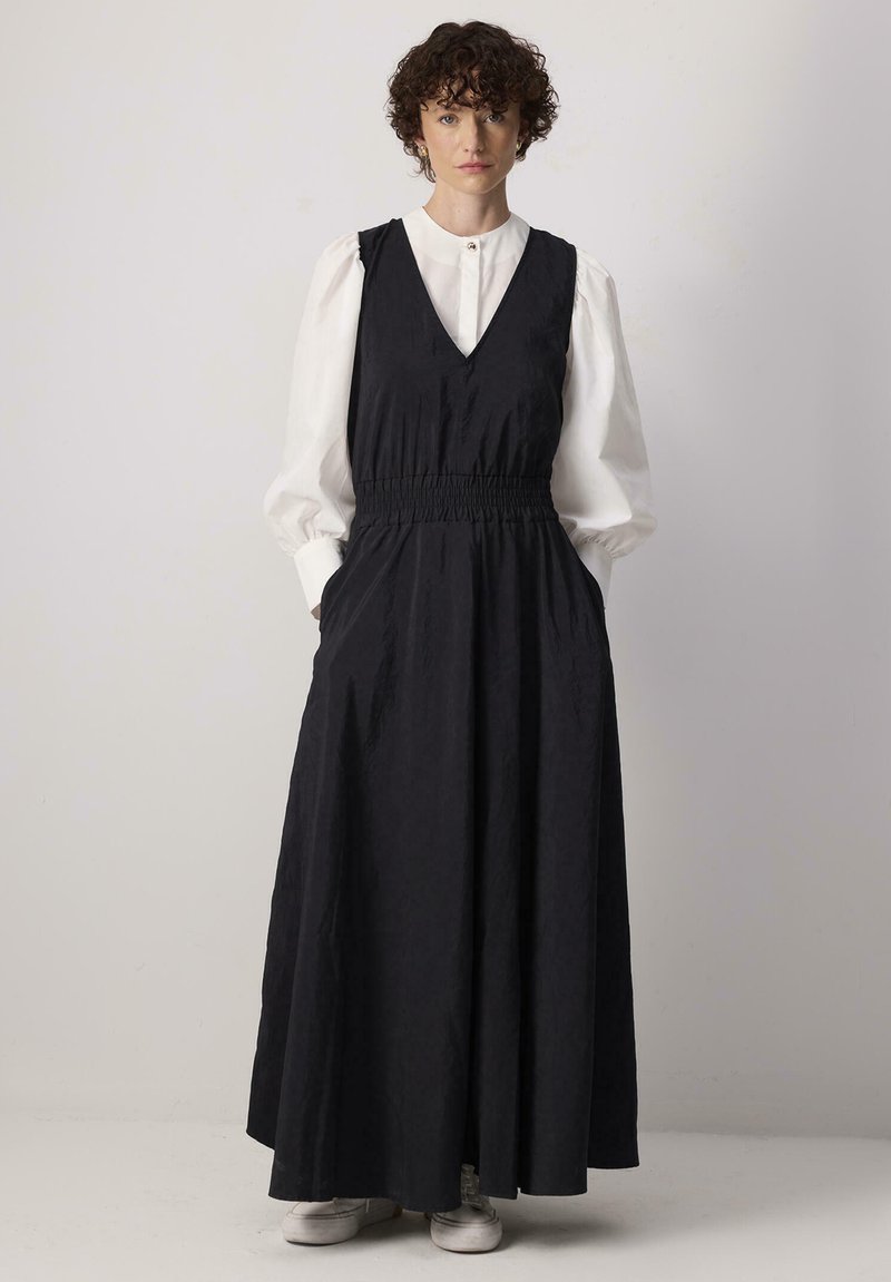 Pikk must kleit, millel on V-kaelus, elastne vöökoht ja küljetaskud. Seljas valge puff-sleeve särk ja kombineeritud valgete tennisetossudega.