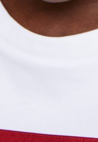 T-shirt bianca con striscia orizzontale rossa nella parte inferiore. Tessuto morbido con scollo rotondo e superficie liscia.