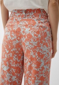 I pantaloni stampati presentano una base arancione con un motivo di foglie azzurre. Il design include due tasche posteriori e una vita aderente.