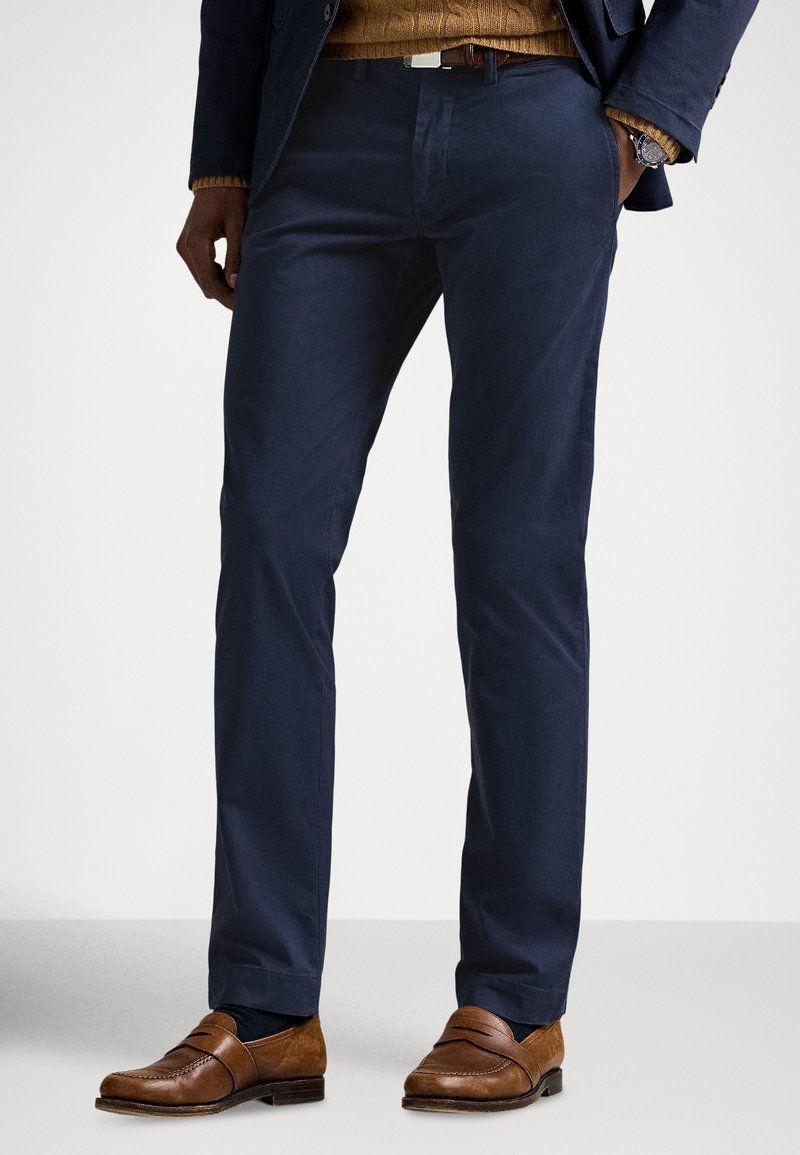 Granatowe spodnie bawełniane o wąskim kroju, zestawione z brązowymi skórzanymi mokasynami o teksturowanym wykończeniu i płaskiej podeszwie.