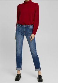 Rød bluse med høj hals og lange ærmer, parret med medium vaskede denim jeans. Sættet har oplyste manchetter og sorte loafers.
