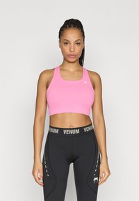 Ružová športová podprsenka so štvorcovým výstrihom a širokými ramienkami, kombinovaná s čiernymi legínami s logom "VENUM" a bielymi bočnými pruhmi.