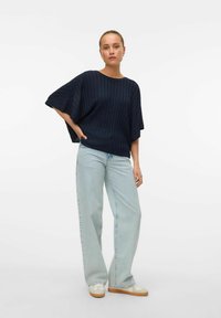 Granatowa bluzka z krótkim rękawem w prążki zestawiona z jasnoniebieskimi spodniami szerokimi w nogawkach i białymi sneakerami z brązowymi podeszwami. Minimalistyczny design, swobodny krój.