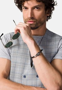 Szary kamizelka w kratę, zestawiona z szarym t-shirtem. Dodatki to zielone okulary przeciwsłoneczne oraz czarna bransoletka z zapięciem.