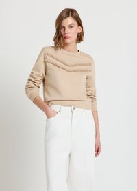 Sweat-shirt beige avec un motif chevron texturé, col rond et poignets côtelés, associé à un jean blanc taille haute.