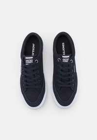 Baskets en toile bleu marine avec semelles en caoutchouc blanc, dotées d'un design à lacets, d'accents cousus et d'une marque sur la languette et le côté.