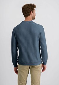 Dunkelblauer Strick-Polo-Pullover mit vertikaler Rippung, langen Ärmeln und geradem Saum, kombiniert mit beigefarbenen Hosen.
