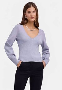 Lichtpaarse ribgebreide trui met een V-hals en lange mouwen, gecombineerd met zwarte broek. Heeft een getailleerd ontwerp en een zachte textuur.