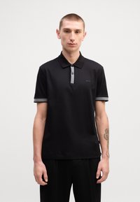 Camisa polo preta com um design sólido, apresentando um colarinho riscado cinza e dois botões. Tecido texturizado com um logotipo discreto no peito.