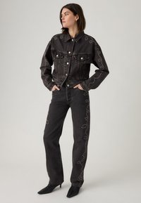 Black denim jacket and pants with silver stud details. Jacket features a collared neck and button front; pants are straight-cut and high-waisted.
