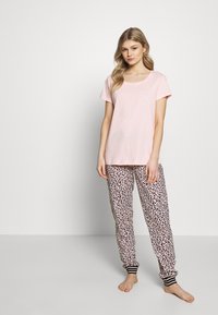 Roze katoenen T-shirt met korte mouwen, gecombineerd met pyjamabroek in luipaardprint. De broek heeft elastische boorden met zwart-witte strepen.
