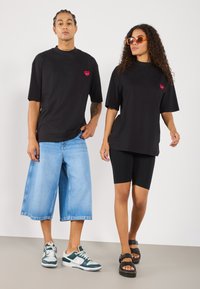 Black t-shirts with a red heart logo, paired with wide denim shorts and black leggings. Sneakers and sandals complete the outfits.