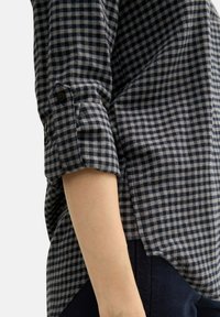 Chemise en flanelle à carreaux bleu marine et gris avec des manches retroussables, dotée de détails en boutons et d'une texture douce. Conçue pour un style décontracté.