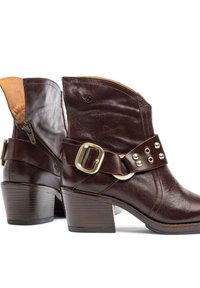 Botas de tobillo de cuero marrón con un tacón apilado, que presentan un acento beis en la parte superior, una cremallera lateral y una correa decorativa con herrajes en tono dorado.