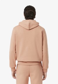 Felpa con cappuccio in morbido tessuto rosa chiaro. Presenta una vestibilità rilassata, polsini a costine e un design con tasca a marsupio nella parte anteriore.