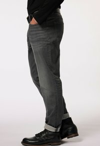 Jeans in denim grigio con vestibilità slim, caratterizzati da una leggera scoloritura, orli arrotolati e tasche laterali, abbinati a stivali neri con lacci.