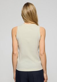 Top senza maniche a coste beige con scollatura rotonda e design aderente, caratterizzato da una texture liscia e da un leggero stretch.