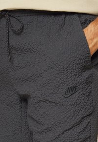 Pantalones cortos negros con textura, cintura con cordón y bolsillos laterales; cuentan con un pequeño logotipo negro de Nike en el frente.