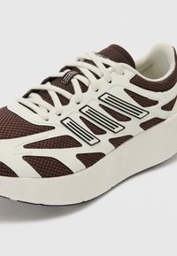 Baskets en maille marron avec des accents synthétiques blancs, présentant une semelle épaisse et des détails noirs, affichant un design moderne et sportif.