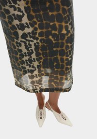 Gonna midi in tessuto trasparente con stampa leopardata, caratterizzata da macchie nere e marroni, abbinata a scarpe slingback bianche con punta a forma di freccia e dettagli con lacci.