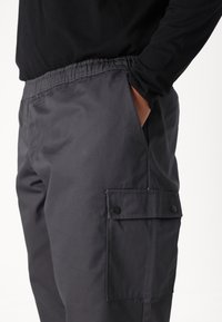 Gray cargo pants with an elastic waistband, side pockets, and a buttoned patch pocket on the thigh. Made from a smooth, durable fabric.
