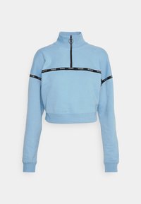 Lichtblauwe cropped sweatshirt met een hoge kraag, een halve rits aan de voorkant en een zwarte logoband over de borst en mouwen. Zachte textuur.