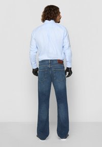 Light blue checkered long-sleeve shirt paired with wide-leg dark blue denim jeans, featuring rear pockets and a brown leather patch.