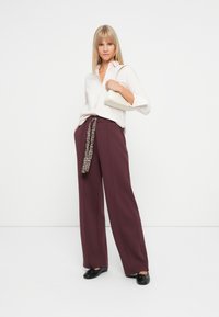 Pantalons larges bourgogne avec une ceinture à imprimé léopard, associés à une chemise blanche à boutons et un petit sac à main blanc. Des ballerines noires complètent le look.