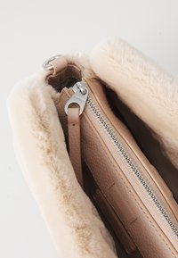 En myk rosa lærveske med en fluffy kremfarget innside, med en sølvglinsende glidel�ås og et lærmerke inni. Designet er kompakt og rektangulært.