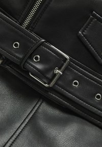 Textura de cuero negro con una hebilla plateada y ojetes metálicos. Presenta una cremallera y un diseño cosido, resaltando su forma estructurada.