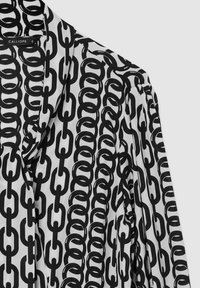 Blusa bianco e nero con un motivo a catena, realizzata in un tessuto morbido con una vestibilità ampia e dettagli del colletto pieghettato.