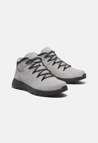 Grå vandringsskor med en slät mocka överdel, svart gummisula, grå snören och logodetaljer. Midsko-design för ankelsupport.