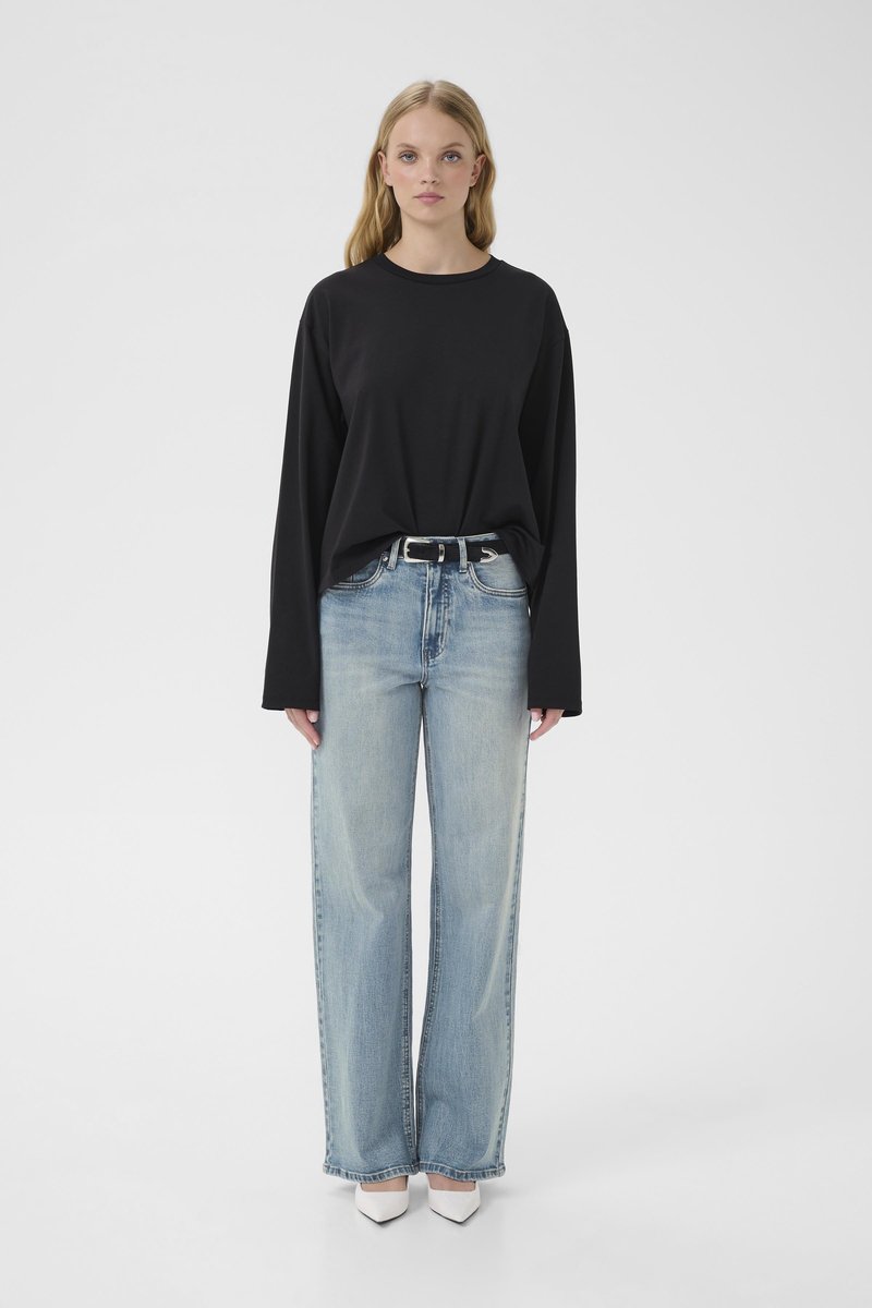 T-shirt noir à manches longues associé à un jean bleu clair à jambes larges et des escarpins blancs à bouts pointus, affichant une coupe décontractée et relax.