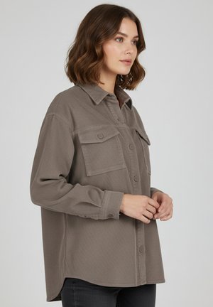 Brown corduroy shirt with a button-down front, two chest pockets, and long sleeves. Textured fabric with a slightly curved hemline.