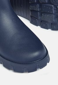 Morske plave gumene čizme s glatkom površinom, robusnom potplatom i debelim, teksturiranim rubom. Naglasak na izdržljivosti i prianjanju za vanjsku upotrebu.