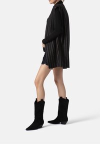 Černá bezrukávová vesta s vertikálními pruhy, spárovaná s černým dlouhým rukávem a černými semišovými kovbojskými botami s propracovaným prošíváním.