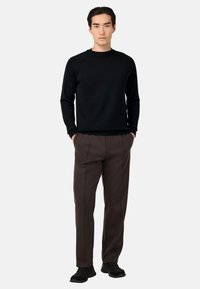 Juodas megztinis su apvalia iškirpte, rudos spalvos prisiūtos kelnės ir juodi sportbačiai. Lygus audinys, laisvas siluetas, minimalistiškas dizainas, jokios matomos raštus.