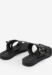 Sandali neri con ampie cinghie sovrapposte e un accento circolare dorato. Suola piatta con un interno testurizzato per una buona aderenza. Design semplice e minimalista.