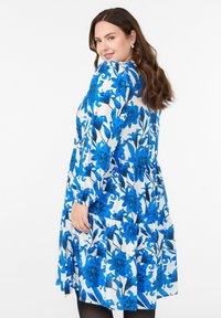 Valge lilleline kleit julgete siniste lillemustriga, pikad varrukad ja kihiline disain. Pehme kangas, millel on lõdvestatud istuvus ja r gathered accents.