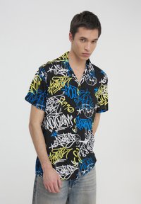 Camicetta a maniche corte nera con vivaci motivi in stile graffiti in bianco, blu e giallo; tessuto leggero con una vestibilità comoda.