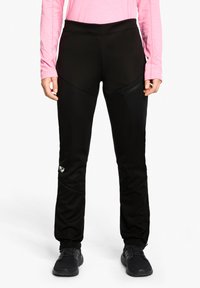 Schwarze Sporthosen mit hohem Bund, Reißverschlusstasche und strukturierten Paneelen, kombiniert mit schwarzen Schuhen und einem pinken Langarmoberteil.