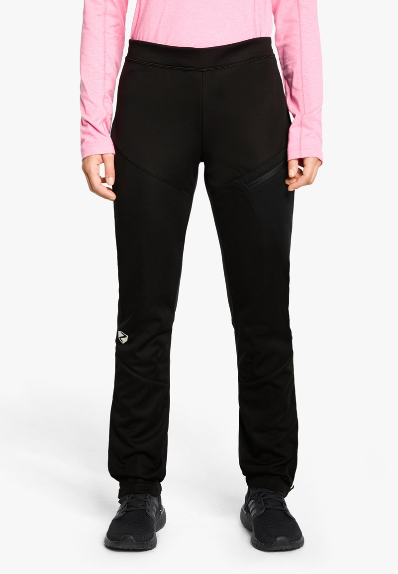 Schwarze Sporthosen mit hohem Bund, Reißverschlusstasche und strukturierten Paneelen, kombiniert mit schwarzen Schuhen und einem pinken Langarmoberteil.