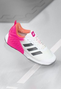 Scarpa sportiva bianca con accenti rosa, tomaia in rete, strisce nere, suola in gomma e colletto imbottito; presenta un design unico della suola intermedia per supporto.