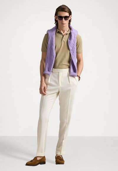 Gai violetas adīta veste virs brūnas polo krekla, apvienota ar baltiem biksēm un brūnām loafers kurpēm. Modelis arī valkā tumšas saulesbrilles.