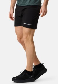 Svart idrottsshorts med en reflektiv rand, tillverkade av lättviktsmaterial. Tillsammans med svarta, ventilerande sneakers med en dämpad sula.