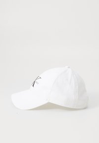 White cotton baseball cap with a curved visor, featuring a black embroidered logo on the front and ventilation holes on the sides.