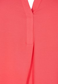 Haut couleur pêche avec un col en V, présentant une surface texturée et un détail de couture centrale. Design simple, sans motifs ou accents supplémentaires.