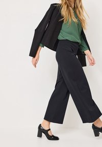 Černý blazer, zelená blůza, námořnické široké kalhoty a černé lakované kožené podpatky. Hladké textury s přizpůsobeným siluetou.